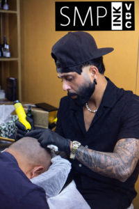 Scalp micropigmentation (SMP) artist performing hairline treatment on a bald client using a yellow SMP machine in a professional studio with SMP INK NYC branding.